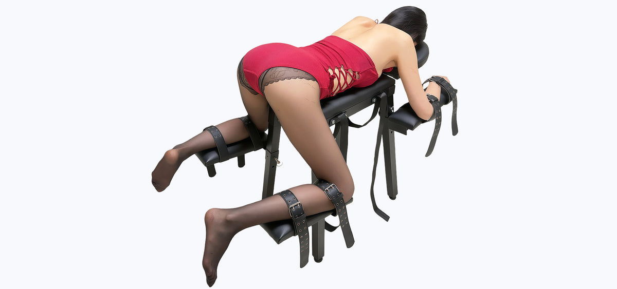 Studio banner product view of the THORN GARDEN Spanking Bench with Straps featuring an ergonomic cushioned metal frame, restraints, and a model in a bondage pose against a white background
