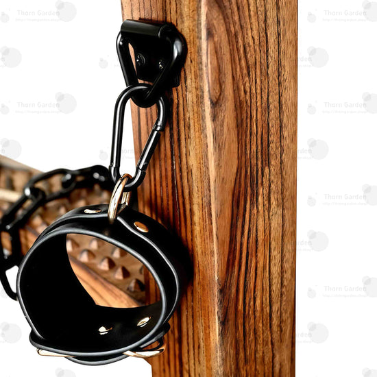 Detail of hand-carved wooden armrests equipped with black metal restraint chains and leather wrist cuffs