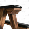 Close-up of padded black leather seat tops with side-mounted metal O-rings and rivet details on wooden bondage bench