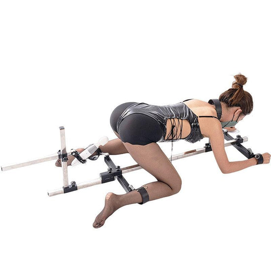 Studio product model angle view of the THORN GARDEN 3G Bondage Stockade with metalcuffs showcasing a model secured in a four-limb restraint rack with an electric sex machine against a clean background